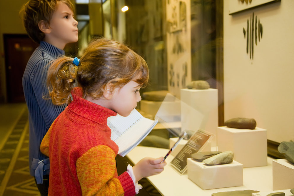 boy and little girl at excursion in historical museum near exhibits of ancient relics in glass cases